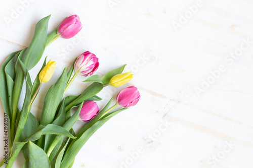 Pink and yellow tulips on white wood background with copy space