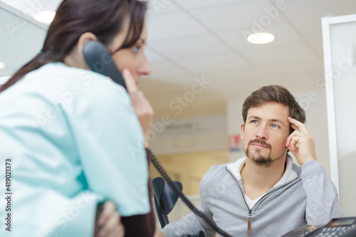 male patient looking at female receptionist using landline phone