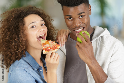 woman eating a pizza and man eating an apple