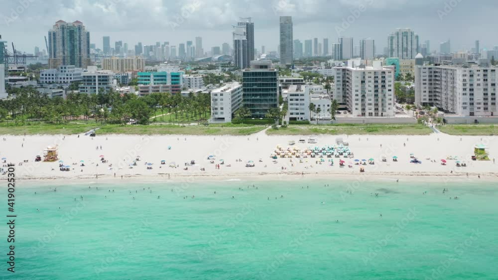 Aerial sand beach with Miami on motion background. People at tropical beach enjoying summer vacation. Crowded beach on sunny day. Perfect footage for travel background. Clear teal Atlantic ocean water Aerial sand beach with Miami on motion background. People at tropical beach enjoying summer vacation. Crowded beach on sunny day. Perfect footage for travel background. Clear teal Atlantic ocean water