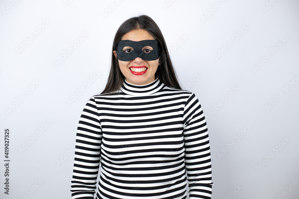 Obraz premium Young beautiful brunette burglar woman wearing mask with a happy face standing and smiling with a confident smile showing teeth