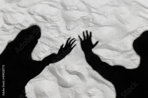 The black silhouette of a guy and a shadow girl stretched their arms forward on the white beach sand background