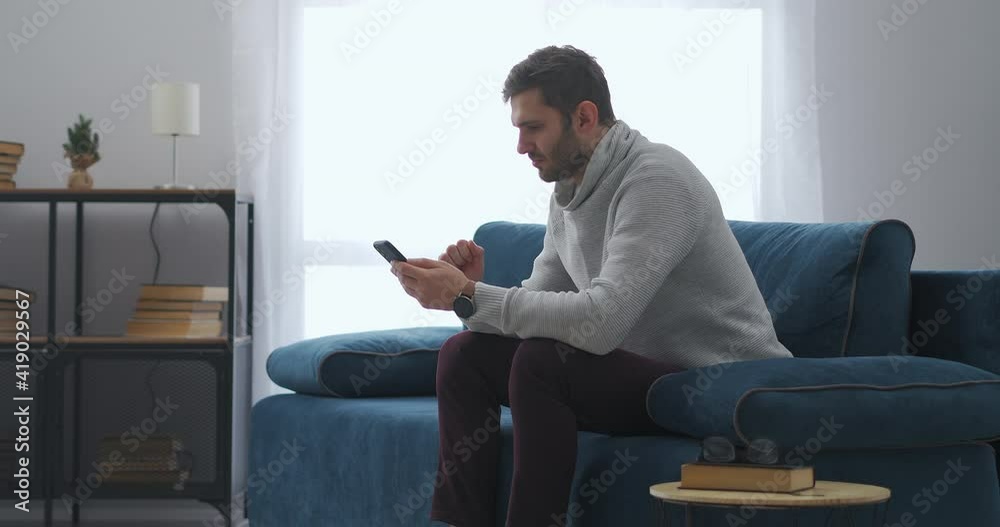 man is using smartphone sitting at home, gambling online in application and winning, rejoicing emotionally man is using smartphone sitting at home, gambling online in application and winning, rejoicing emotionally