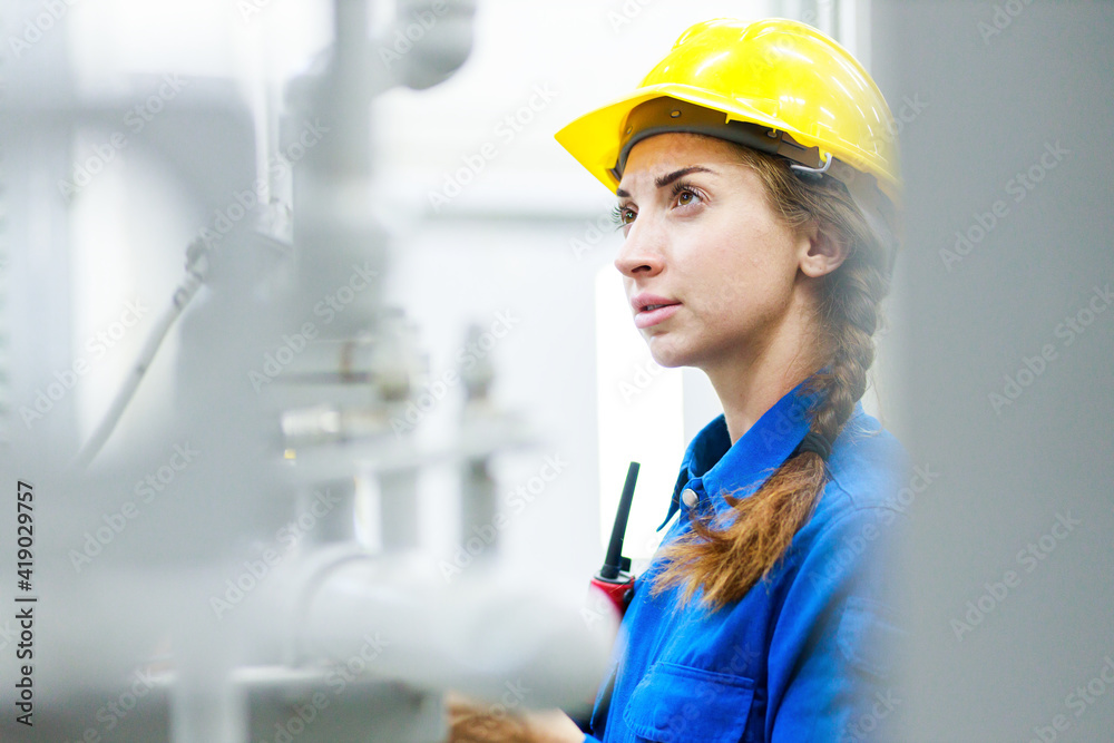 Portrait of young engineer with white helmet looking up and seen from the industrial electronic cable reel in factory warehouse. She is testing and working double check system cooler for freezer room