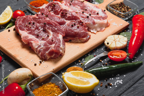 Raw pork meat on wooden cutting board at kitchen table for cooking pork steak roasted or grilled with ingredients herb and spices , Fresh pork