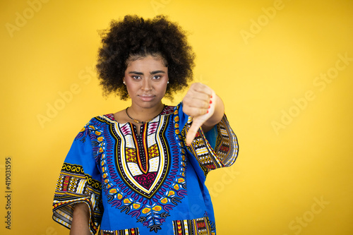 African american woman wearing african clothing over yellow background with angry face, negative sign showing dislike with thumb down