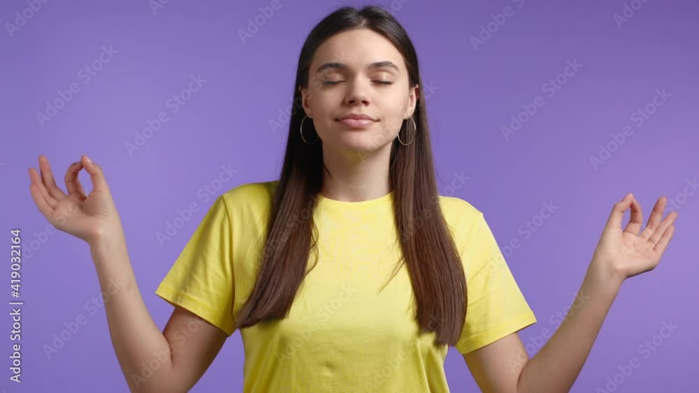 Calm woman in yellow relaxing, meditating. She calms down, breathes deeply with mudra om on violet studio background. Yoga concept. Calm woman in yellow relaxing, meditating. She calms down, breathes deeply with mudra om on violet studio background. Yoga concept.