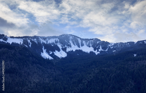 Snow capped mountain in late winter, sunlight breaks through clouds