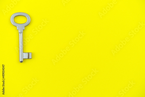 Bodegón que presenta una llave reluciente de tipo antiguo posada a la izquierda sobre un fondo amarilla similar al de una nota o pósit. photo