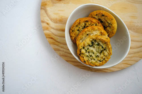 Toma en primer plano de un cuenco blanco con rebanadas de pan tostado con aceite, ajo y perejil cuya textura y aspecto crujiente estimulan el apetito. photo