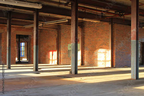 Interior view of an old  run-down  and abandoned factory building. Big  empty room with brick walls  exposed beams  and florescent light fixtures hanging form the ceiling.