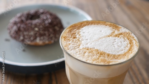 Plant based cappuccino served in a glass with doughnut covered with chocolate sprinkles 