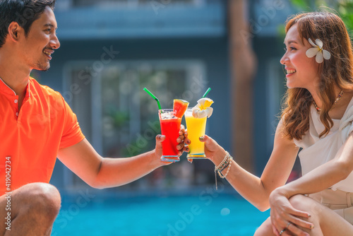 couple sitting by resort and hotel pool together with glass of fruit juice on hand photo