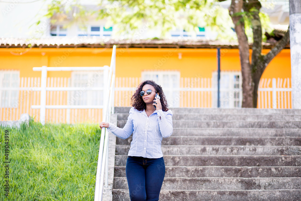 Young black woman walking down a staircase and talking on the phone in a public place Young black woman walking down a staircase and talking on the phone in a public place