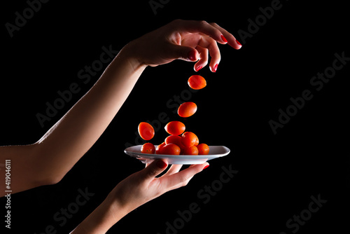 Cherries tomatoes, falling from hands, on a plate with black background and high contrast.Cherries tomatoes on black background.