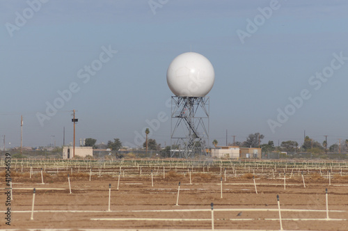 Doppler weather radar tower with a spherical radome on a metal framework, used for atmospheric monitoring and storm detection, situated near agricultural fields and suburban infrastructure in Arizona