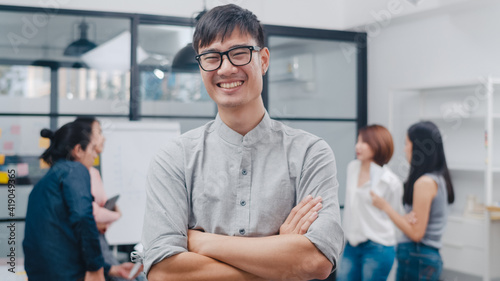 Portrait of successful handsome executive businessman smart casual wear looking at camera and smiling  arms crossed in modern office workplace. Young Asia guy standing in contemporary meeting room.