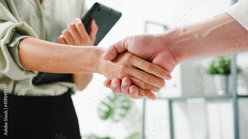 Multiracial group of young creative people in smart casual wear discussing business shaking hands together and smiling while standing in modern office. Partner cooperation  coworker teamwork concept.