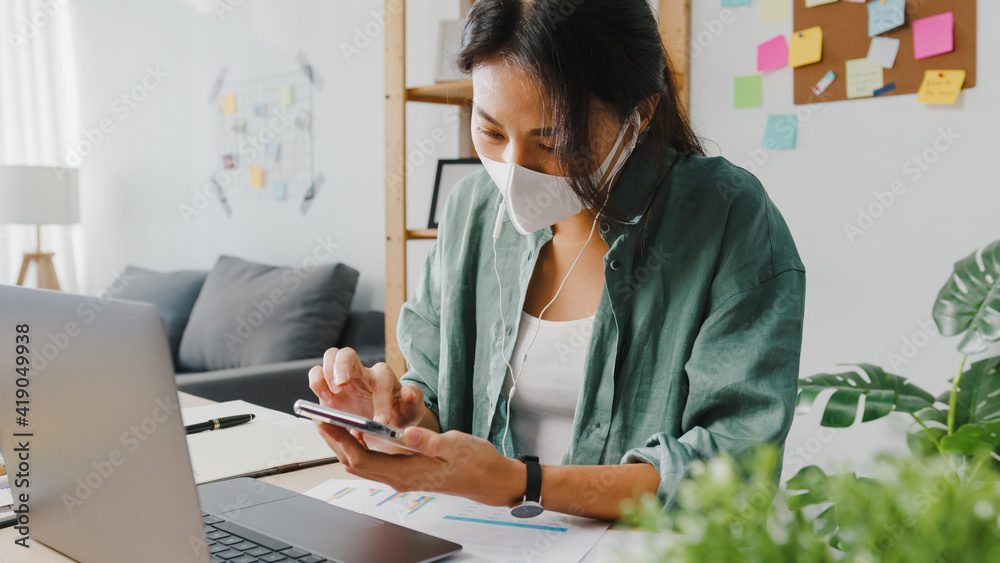 Freelancer Asia women wear face mask using smartphone shopping online via website while sitting at desk in living room. Working from home, remotely work, social distancing, quarantine for coronavirus. - obrazy, fototapety, plakaty 