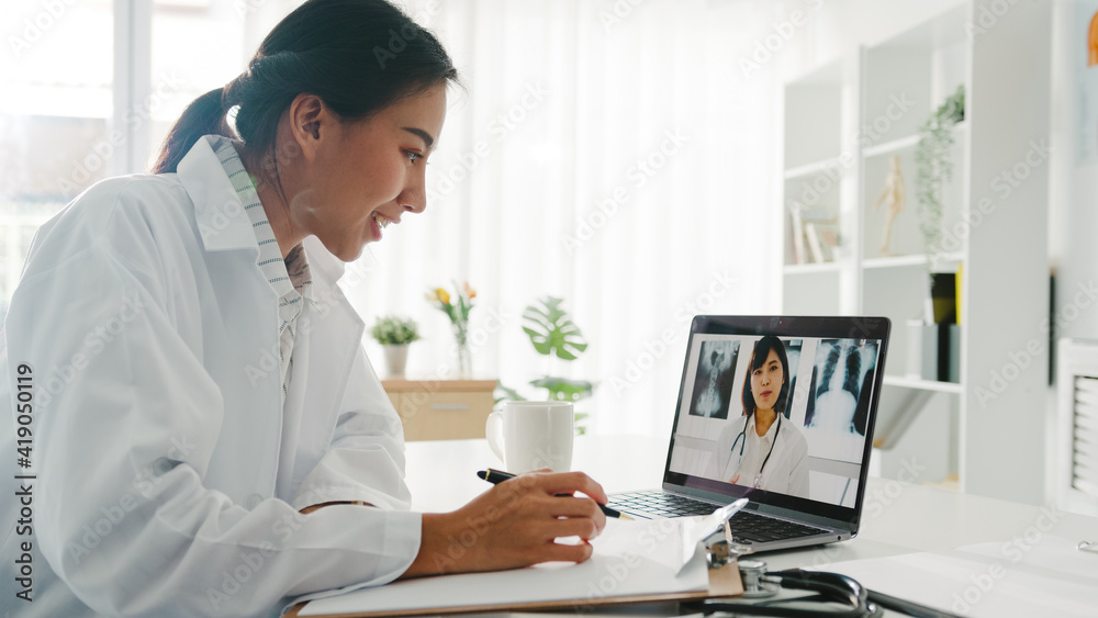Young Asia lady doctor in white medical uniform using laptop talking video conference call with senior doctor at desk in health clinic or hospital. Social distancing, quarantine for corona virus. Young Asia lady doctor in white medical uniform using laptop talking video conference call with senior doctor at desk in health clinic or hospital. Social distancing, quarantine for corona virus.