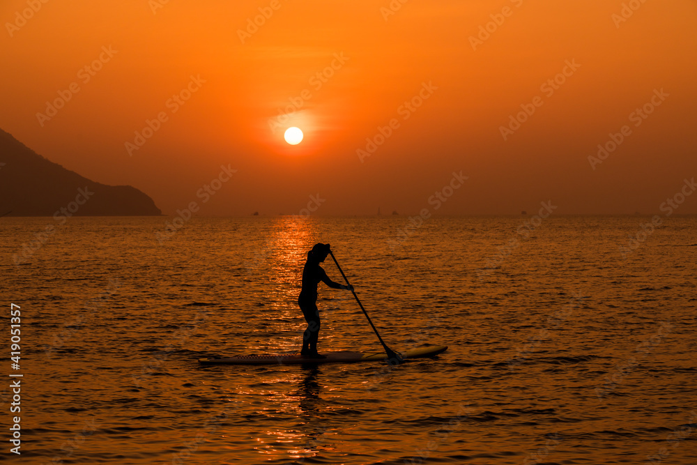 Silhouette sport stand up paddling on sup board or surfboard enjoy to play extreme sport on holidays at sunlight beach.