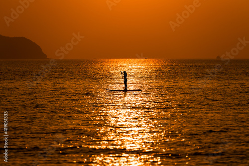 Silhouette sport girl stand up paddling on sup board or surfboard enjoy to play extreme sport on holidays at sunlight beach.