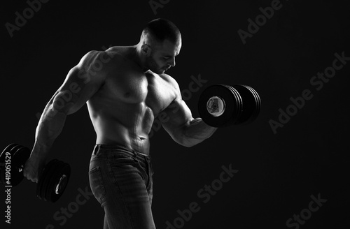 Muscular strong well built men bodybuilder is working out, lifting dumbbells, doing exercises for biceps in gym over dark back ground with copy space. Young man lifting weights. Black and white  © Dmitry Lobanov