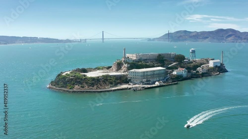World famous touristic landmarks and attraction 4K. Aerial close up Alcatraz island with Golden Gate bridge on background. Historic prison building in green San Francisco bay area waters on summer day