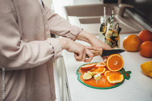 Close up photo of a caucasian woman slicing fruits in the kitchen and preparing a mojito