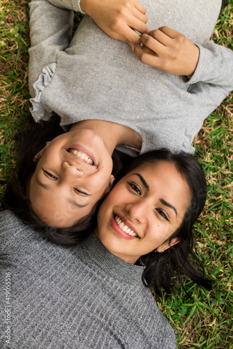 Vertical photography of young latin mother and her daughter lying on the grass.