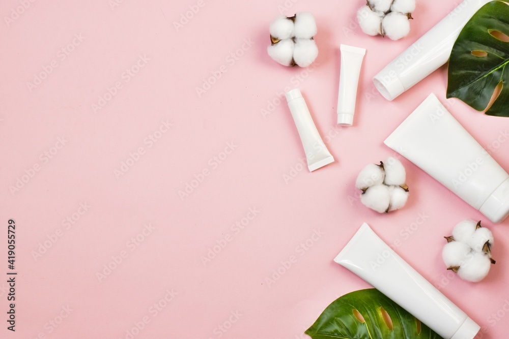 Natural spa cosmetics. White tubes on pink background with cotton flowers.green leaves. Copy space. Flat lay. advertising. mockup. Natural spa cosmetics. White tubes on pink background with cotton flowers.green leaves. Copy space. Flat lay. advertising. mockup.