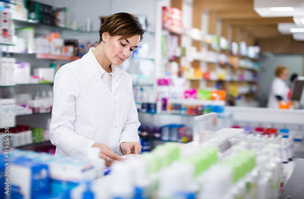 Happy female pharmacist arranging assortment of products in pharmacy