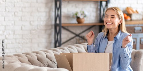 Happy young woman sitting on the couch and unpacking the long-awaited parcel photo