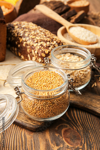 Jars with different cereals and bread on wooden background