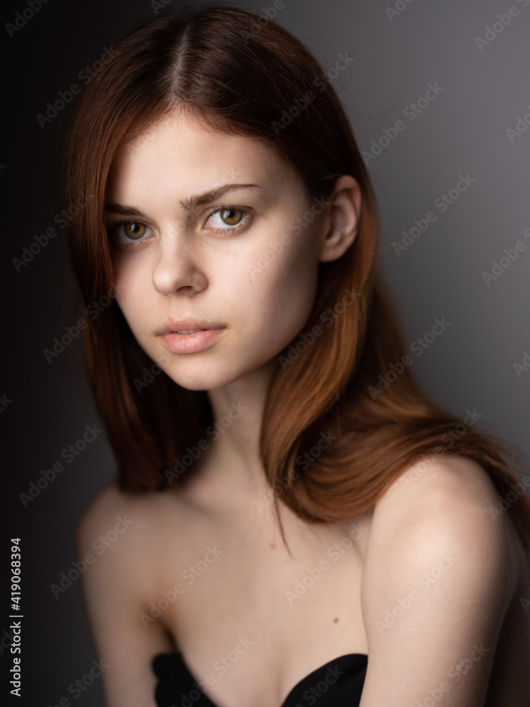 Red-haired woman with bared shoulders portrait close-up dark background model