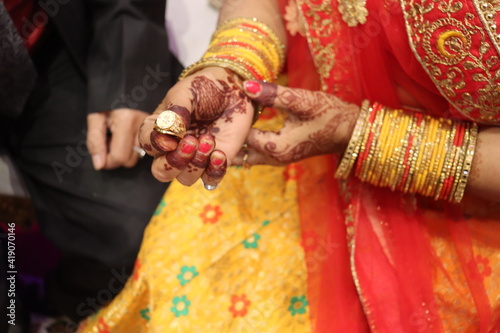 New Delhi, Delhi India- February 28 2021: Ring ceremony and the wedding function of the Hindu Indian couple holding gold ring with diamond. Royal bangles covering hands with traditional tattoo- Mehndi
