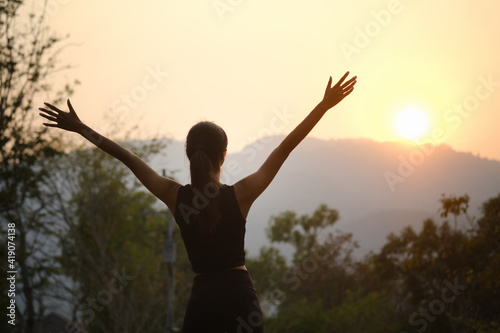 Young sporty woman cheering and celebrating after evening jogging outdoor at sunset in park.
