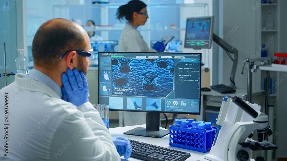 Worried chemist doctor working on pc examining vaccine evolution in scientific modern equipped laboratory. Scientist stuff using high tech and technology researching treatment against covid19 virus