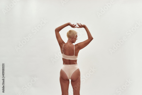 Love yourself at any age. Rear view of a mature woman in underwear keeping arms over the head while posing half naked against light background