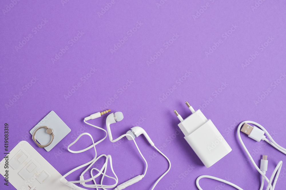 a set of accessories for a smartphone, charger, headphones, holding a ring, adapters for sim cards on a purple background copy space