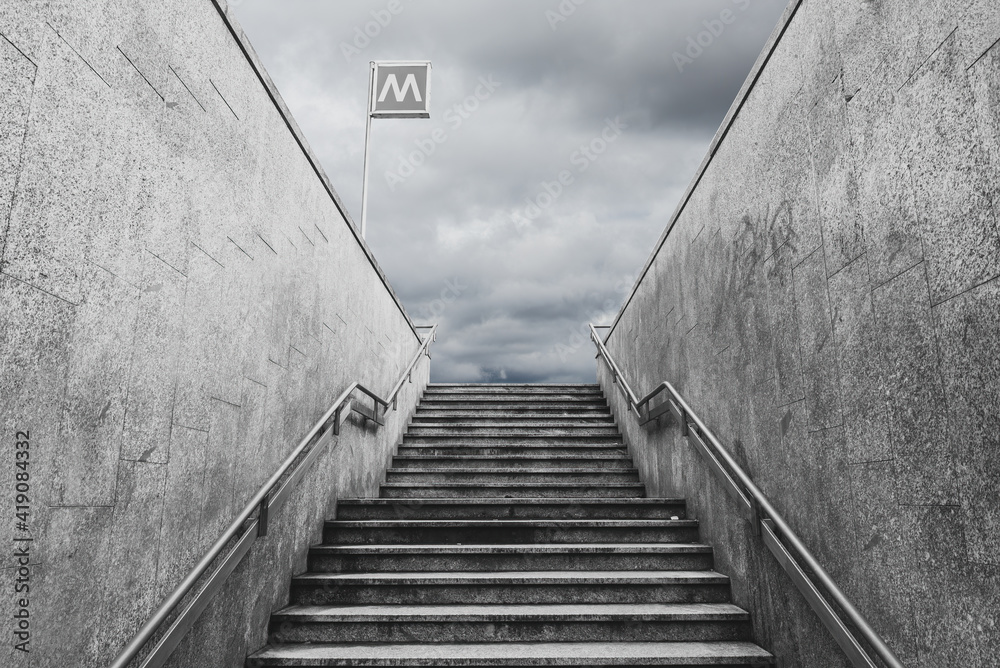 Perspective of the exit staircase of a Milan underground station. Dramatic clouded sky on the background. Monochromatic. Perspective of the exit staircase of a Milan underground station. Dramatic clouded sky on the background. Monochromatic.