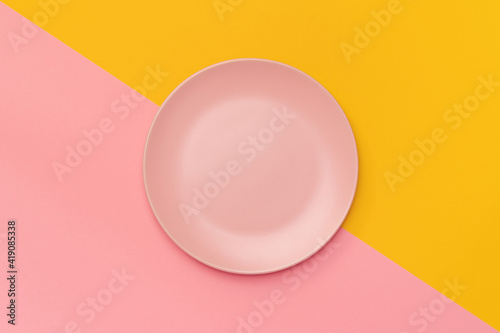 Pink plate on a background divided diagonally into pink and yellow. Minimalism. Minimal cooking concept