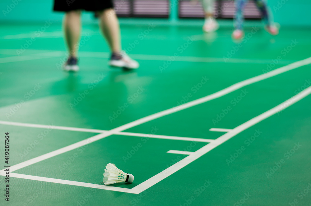 White badminton shuttlecock on a green floor. badminton courts with players competing.