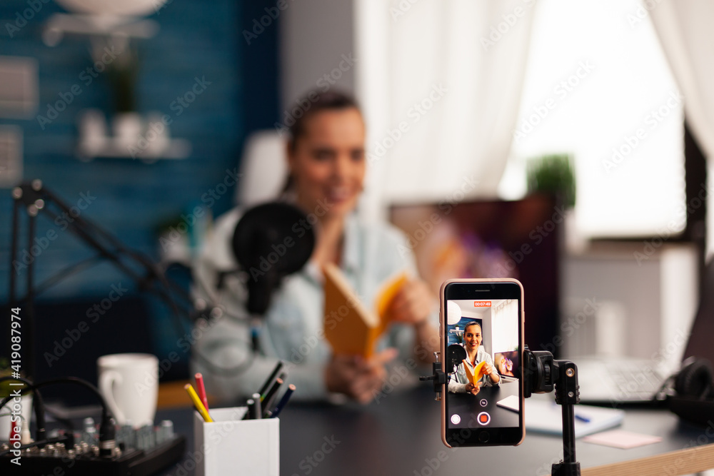 Vlogger holding book during podcast review on social media. Creative content creator influencer streaming live video, recording digital social media communication for her audience - obrazy, fototapety, plakaty 
