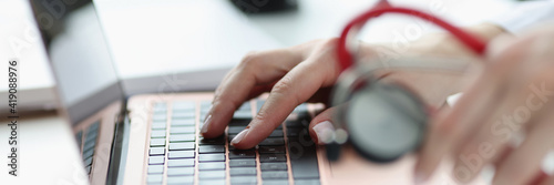 Doctors hands holding stethoscope and typing on keyboard closeup