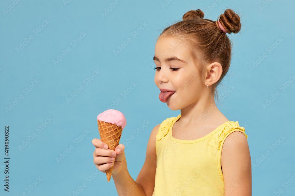 happy little girl eating ice cream in a waffle cone on blue background