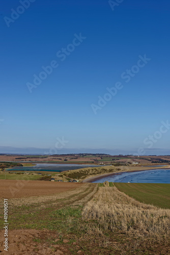 The curving coastline of Lunan Bay seen from the arable Farm Fields on top of the Cliffs towards Arbroath  on a bright day in March.
