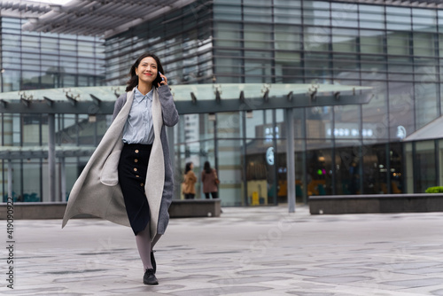 happy young asian business woman talking on the mobile phone walking in the office building