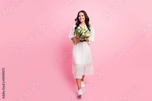 Full body photo of charming cute nice young woman walk look empty space hold flowers isolated on pink color background