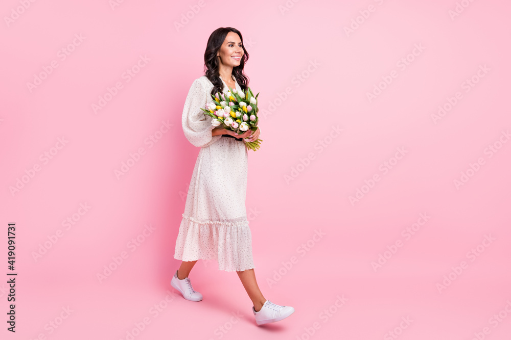 Full size profile side photo of happy young woman walk empty space hold hands flowers weekend isolated on pink color background